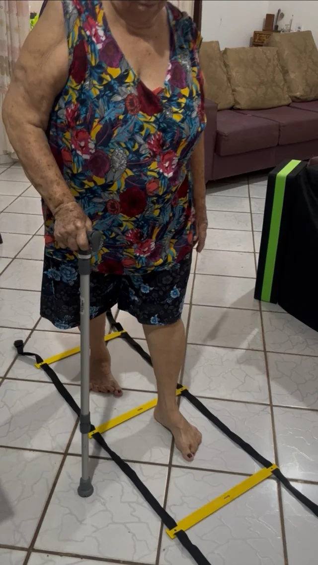 Pessoa realizando atividade de marcha com bengala e uma escada de agilidade posicionada no chão.